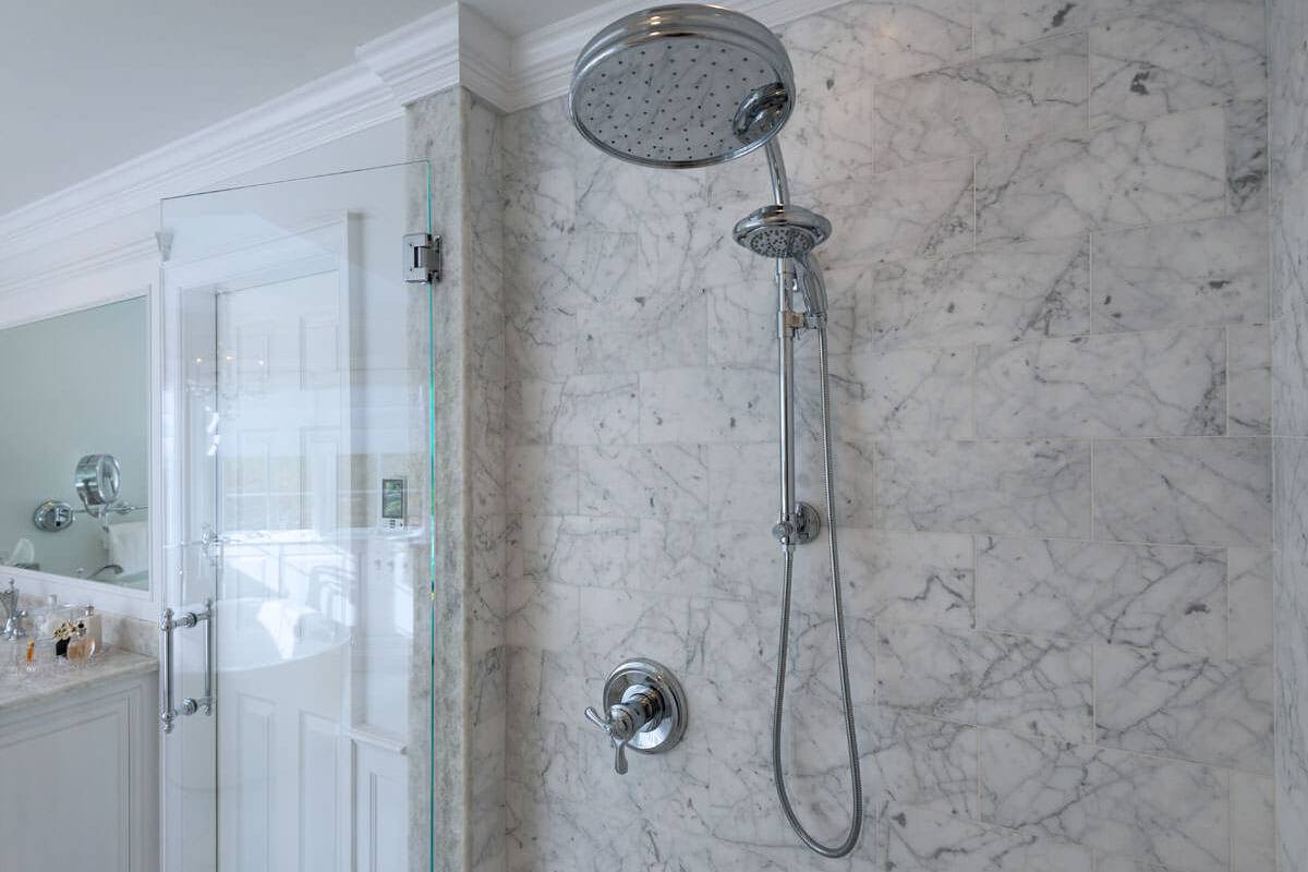 Silver-tone rain head and handheld against a Carrara marble shower wall