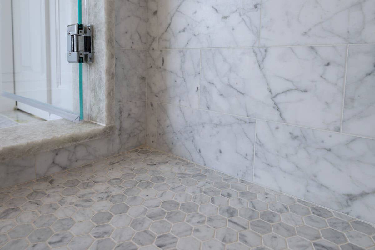 Hexagon mosaic shower floor meeting Carrara marble walls