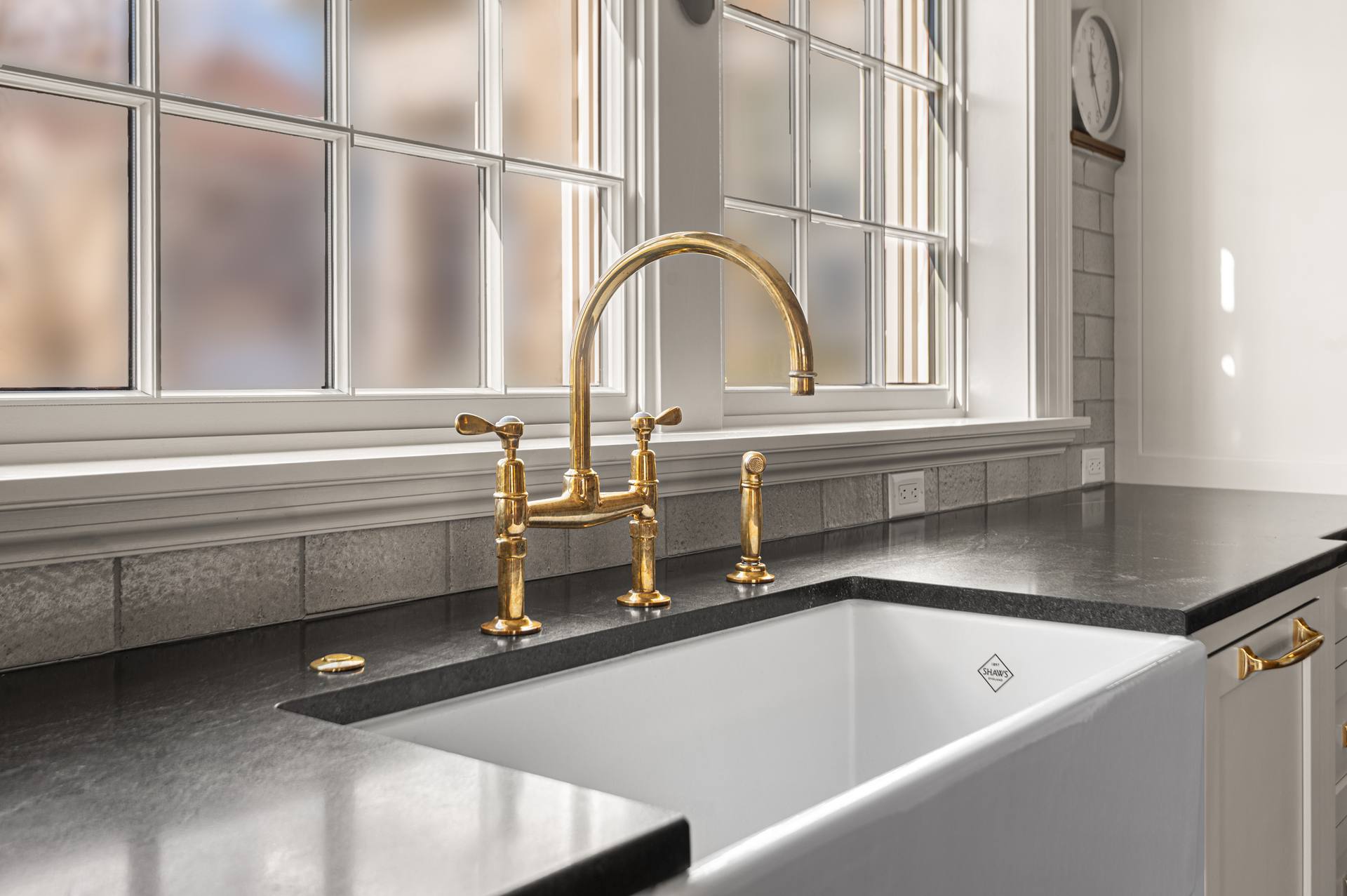 Gold-tone bridge faucet above a white apron sink in a Black Absolute granite counter