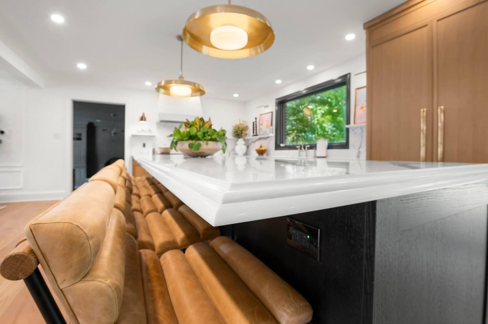 Thick shaped edge on a Calacatta Corchia quartz island beside tan upholstered stools