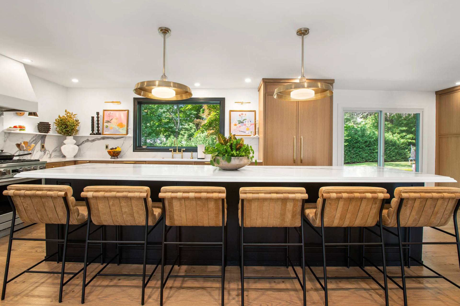 Calacatta Corchia quartz island with tan upholstered stools under gold-tone pendants