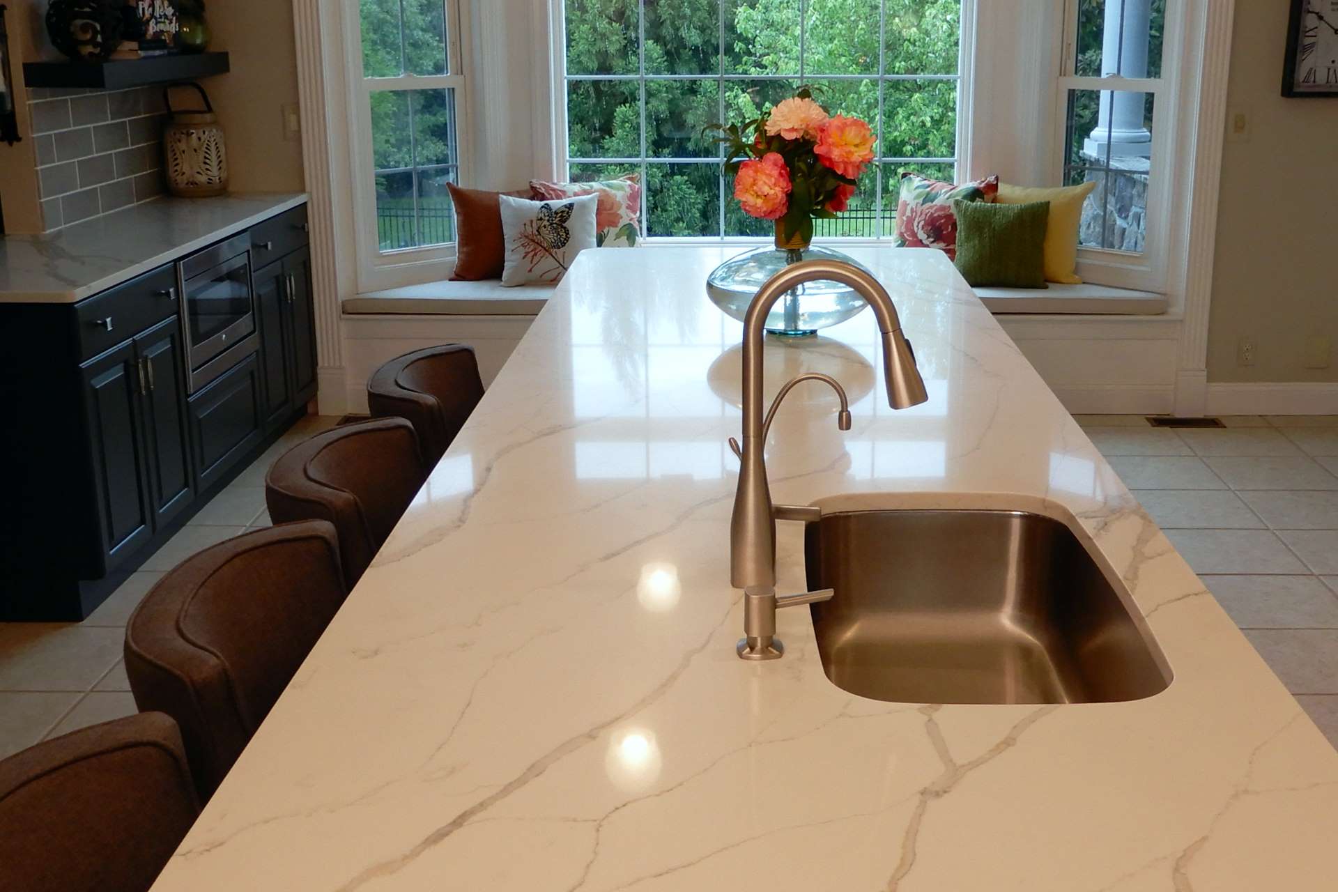 Long Calacatta Gold quartz island with an undermount sink and dark cabinets