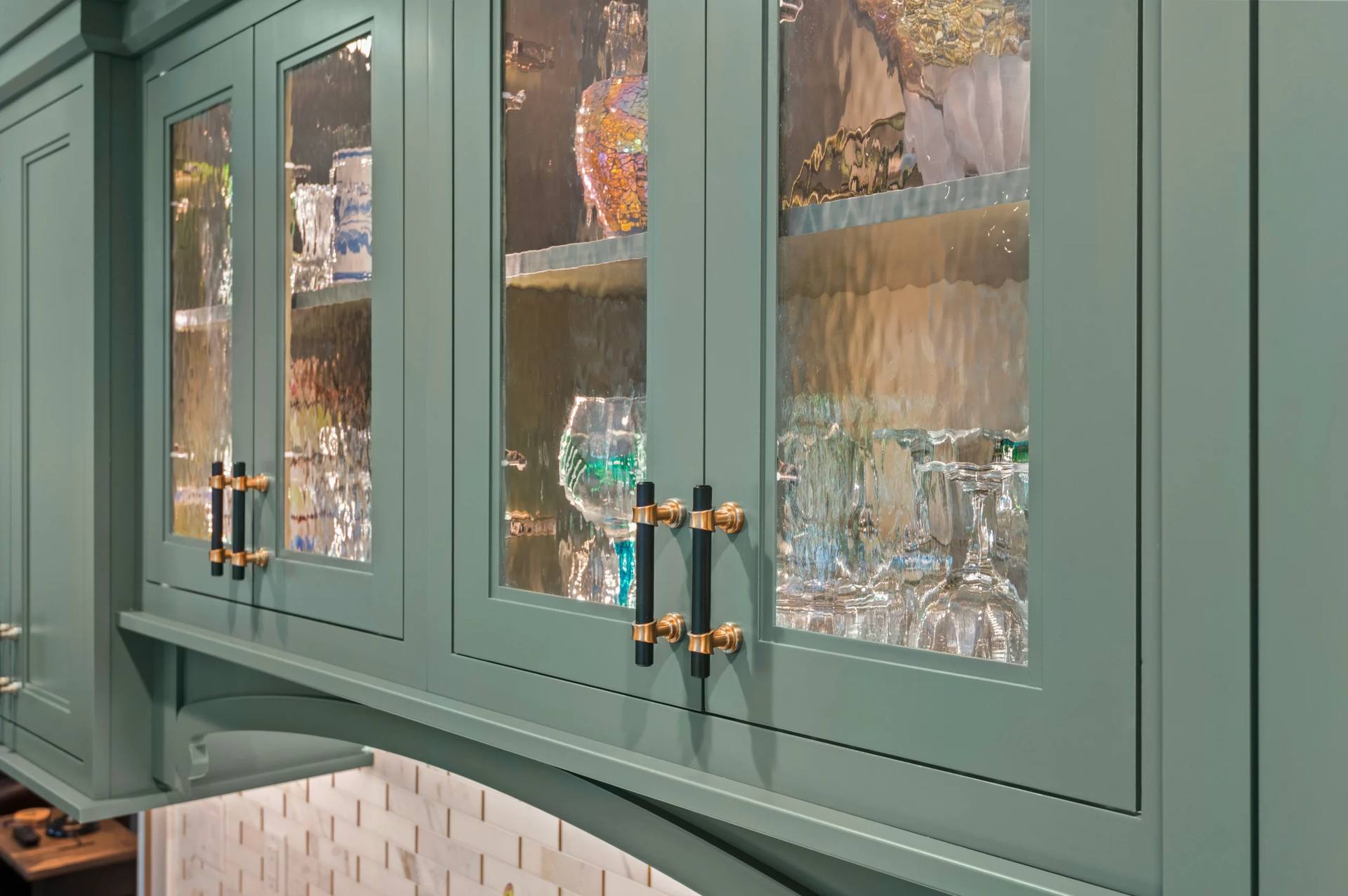 Glass-front green cabinets above a Cambria Windsor Brass quartz counter