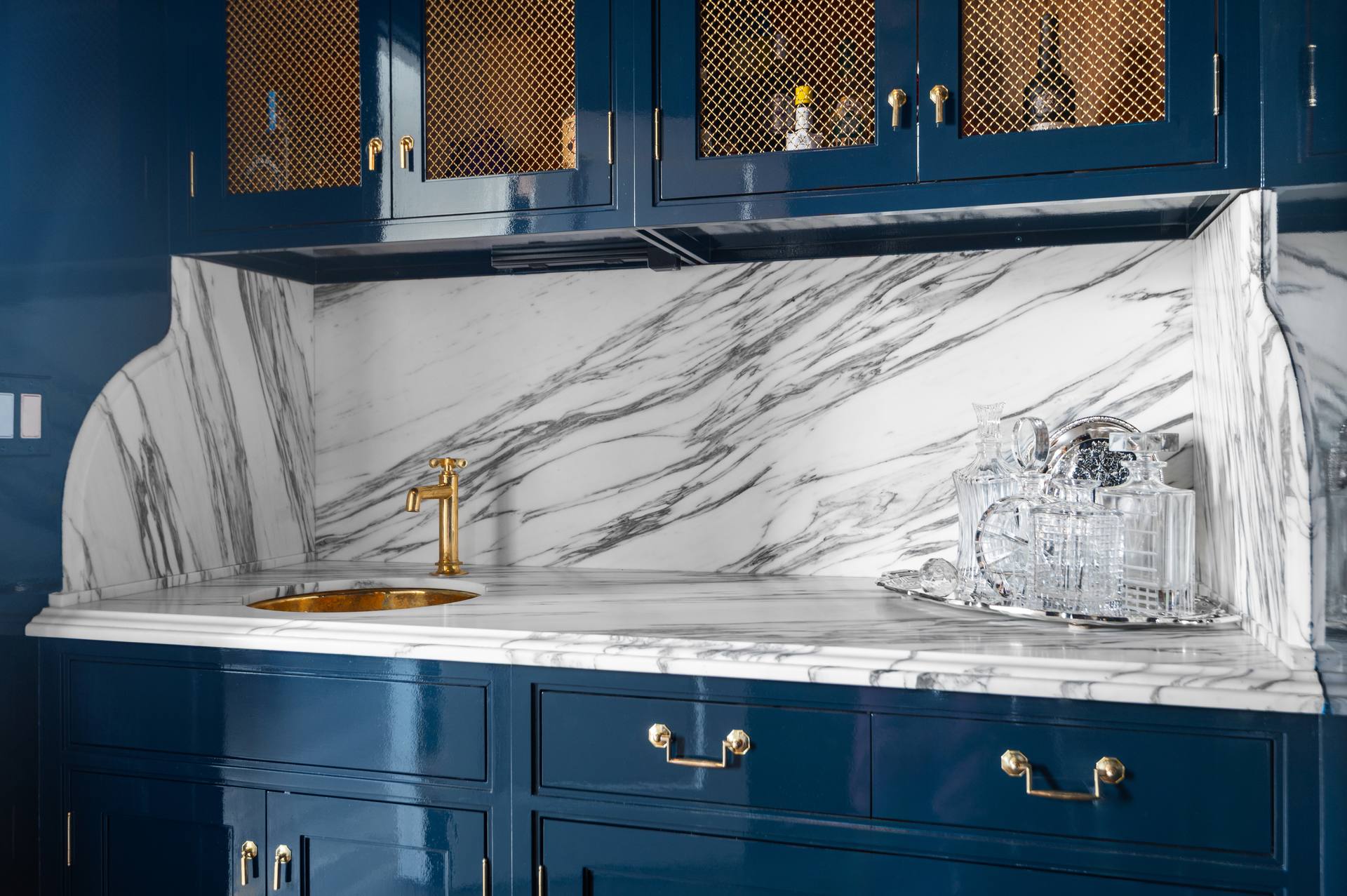 Calacatta Corchia marble bar counter below navy cabinets with gold-tone mesh fronts