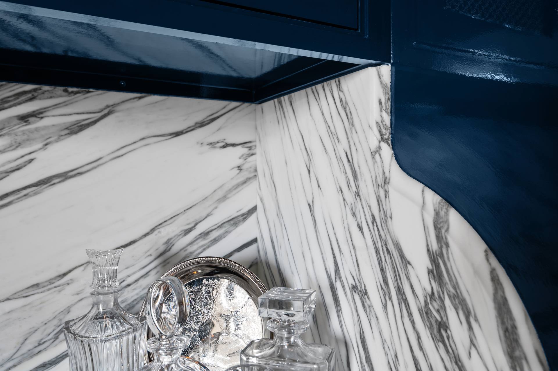 Curved upper edge of a Calacatta Corchia marble backsplash against navy cabinetry
