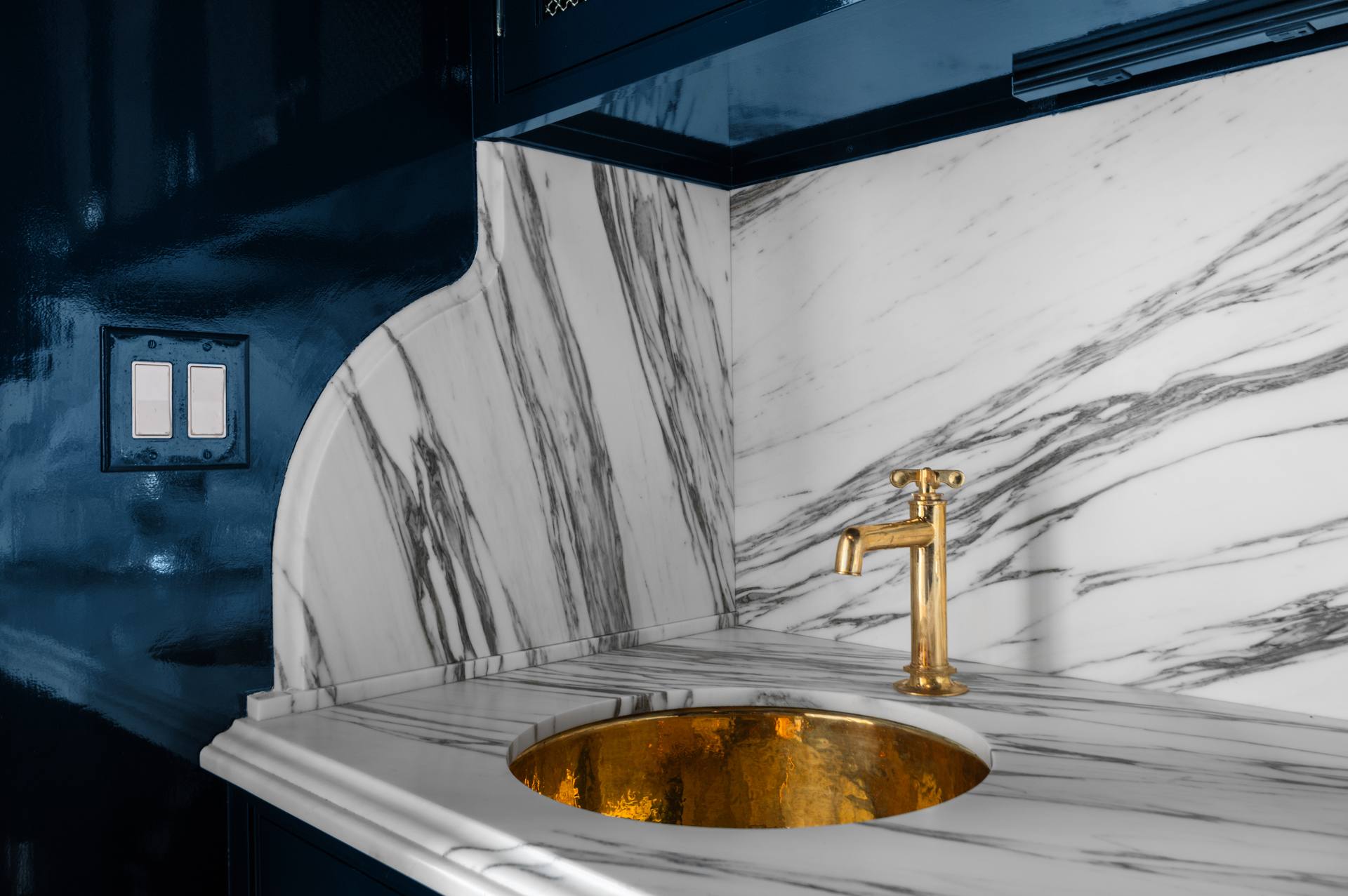 Gold-tone bar sink below the curved edge of a Calacatta Corchia marble backsplash