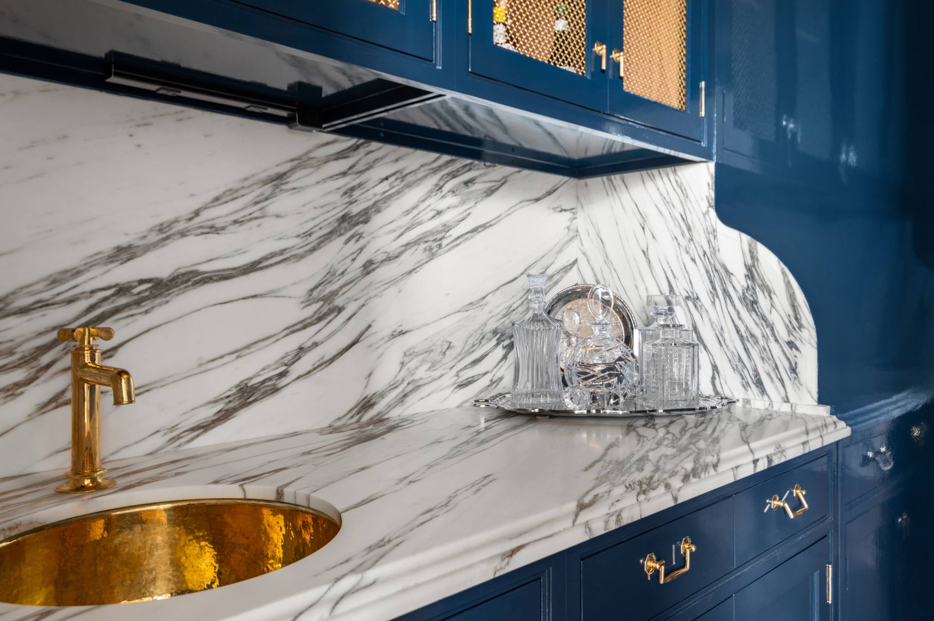 Gold-tone bar faucet above a hammered gold-tone sink in marble