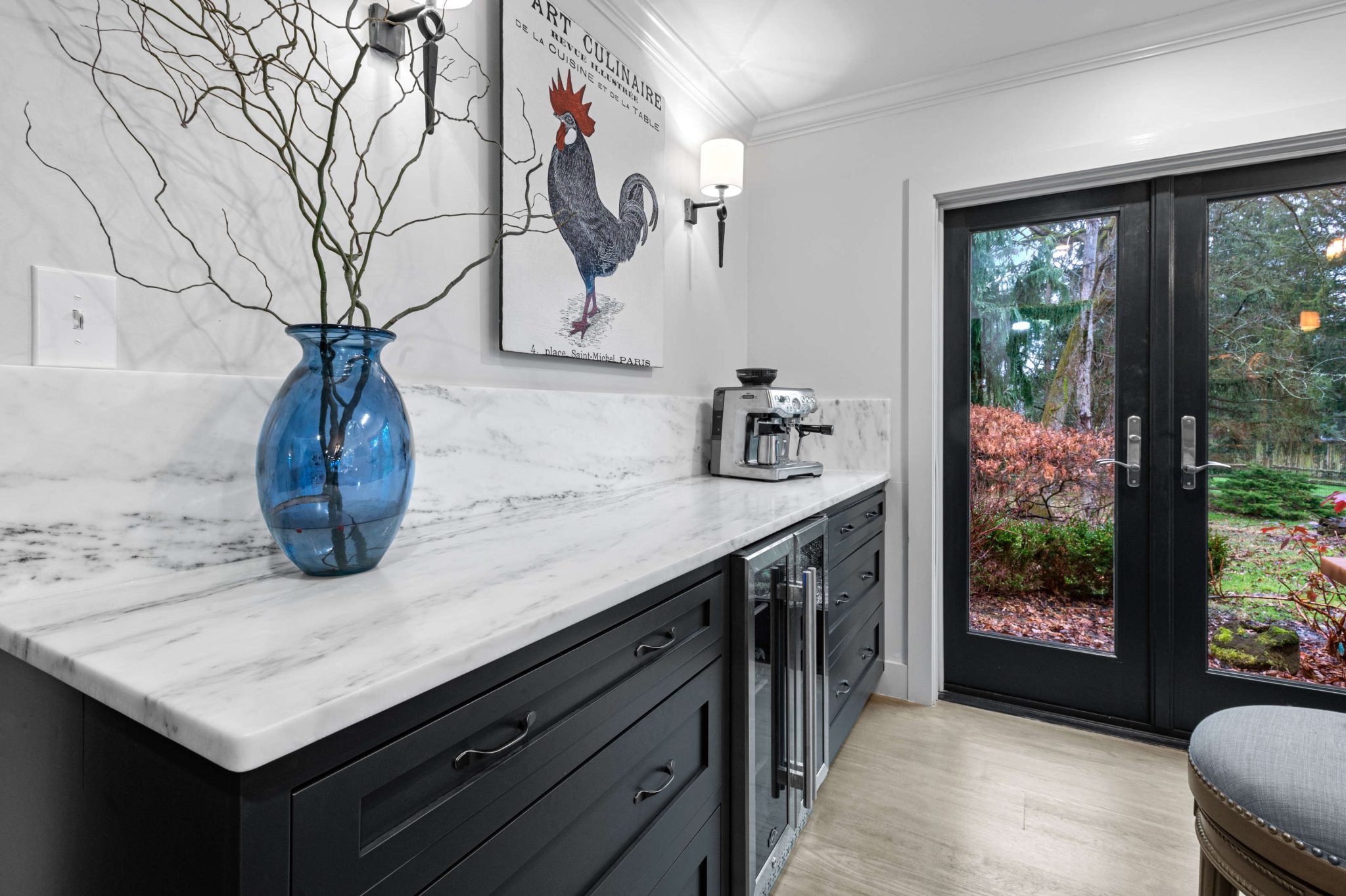 White stone countertop and backsplash with a blue glass vase above dark cabinetry
