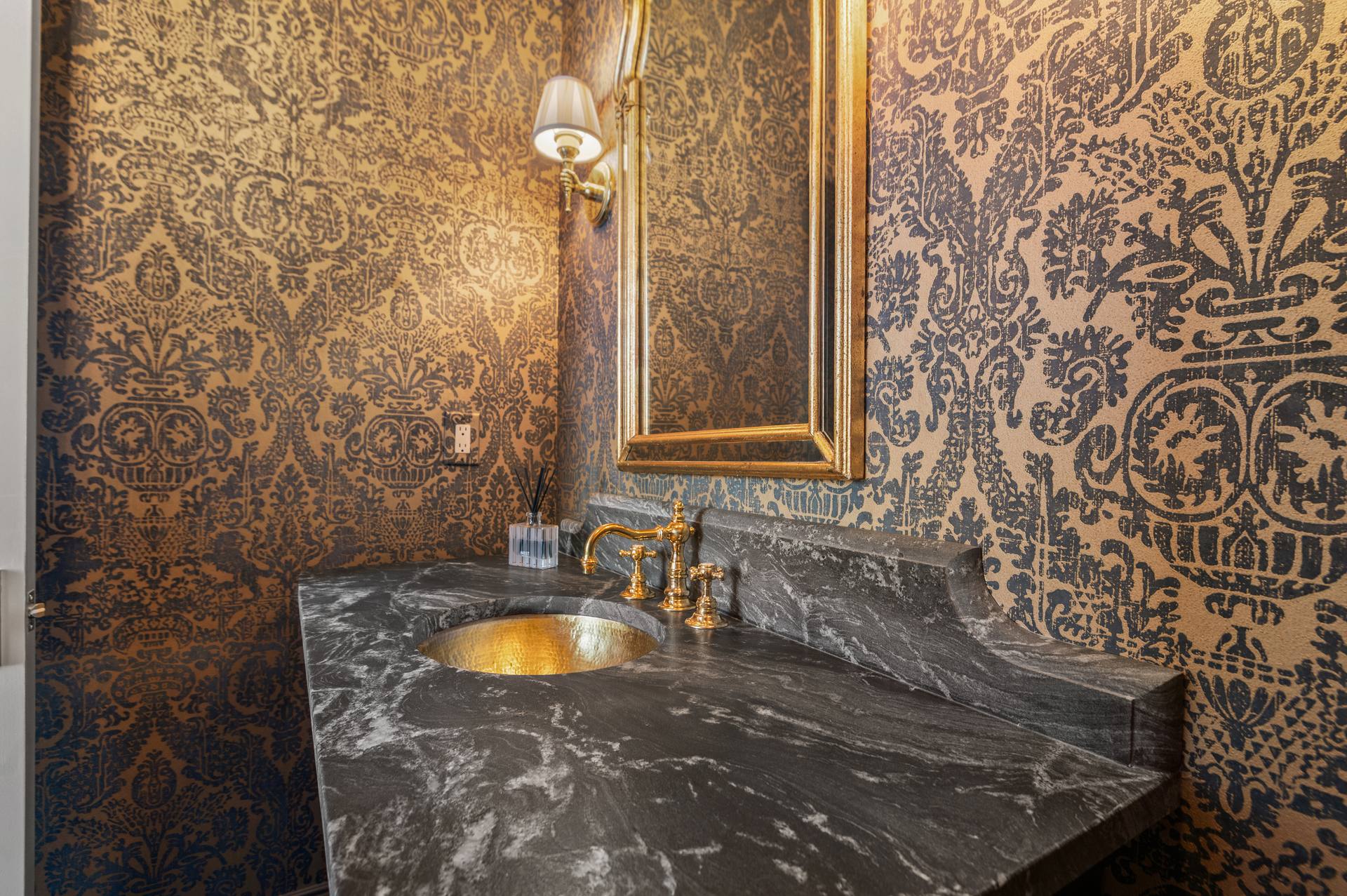 Shaped leathered granite backsplash below a gold-tone wall sconce