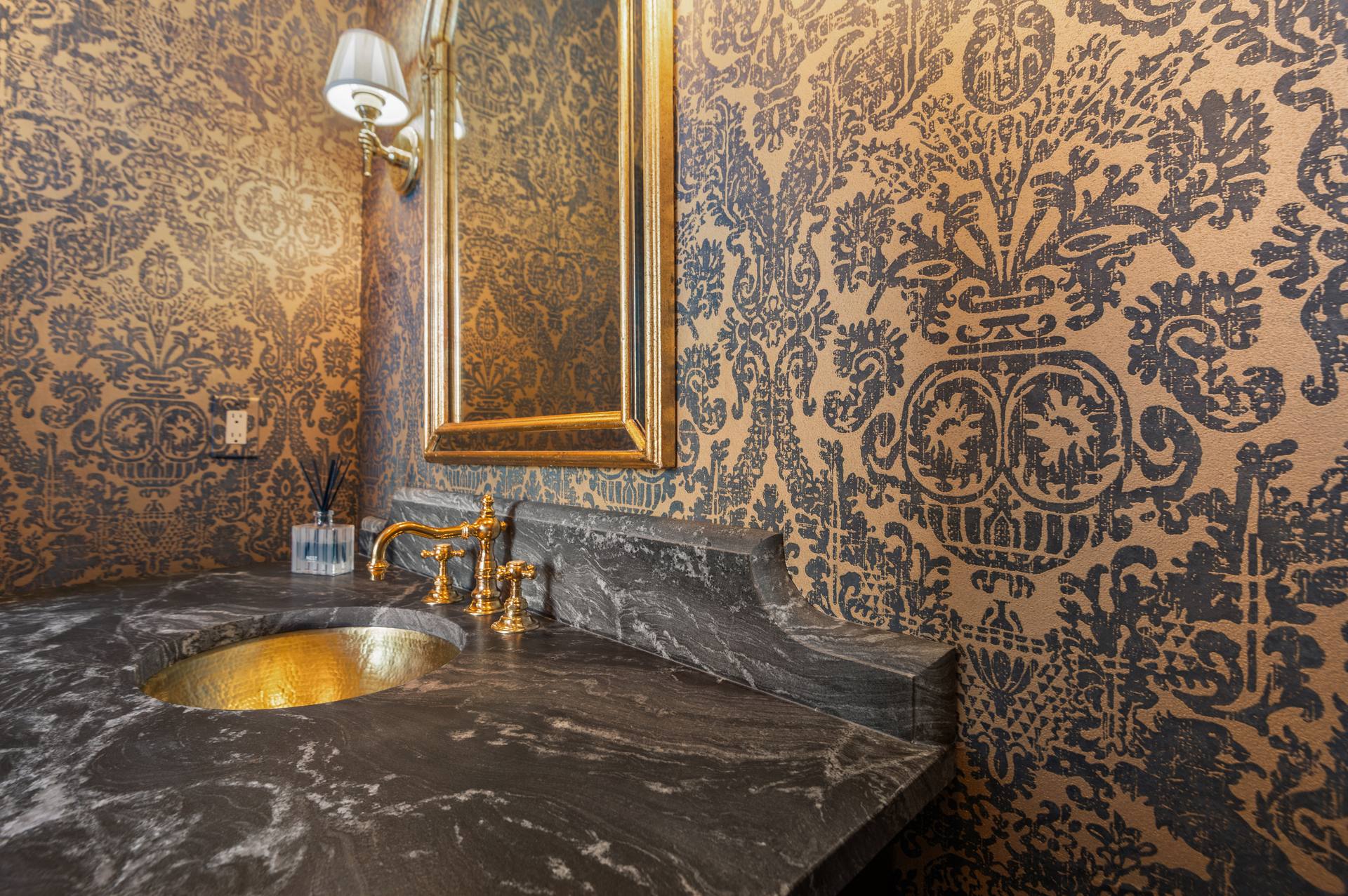 Hammered gold-tone basin in a leathered granite top below a gold-framed mirror
