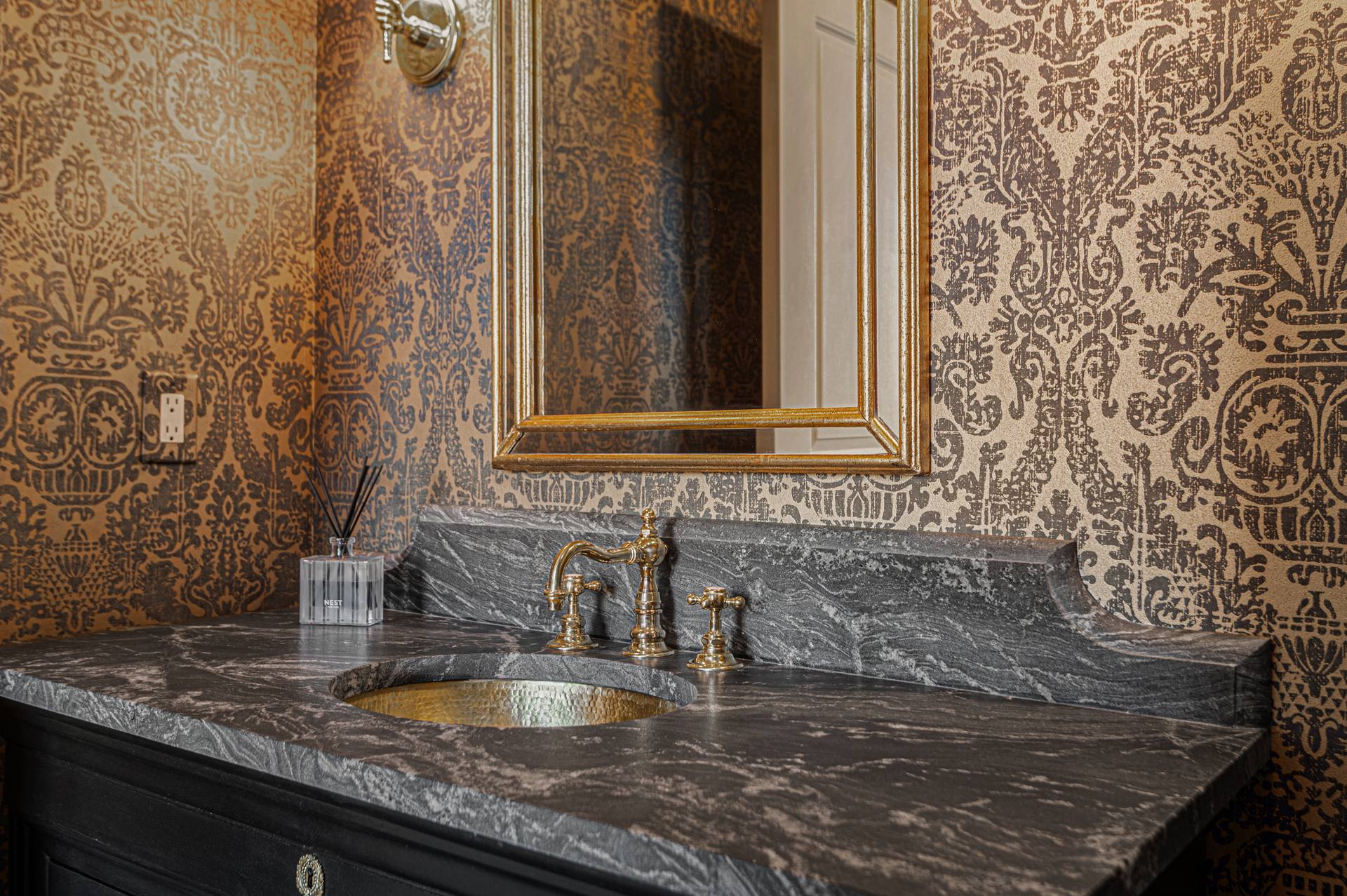 Leathered granite vanity top with a gold-tone basin below a gold-framed mirror