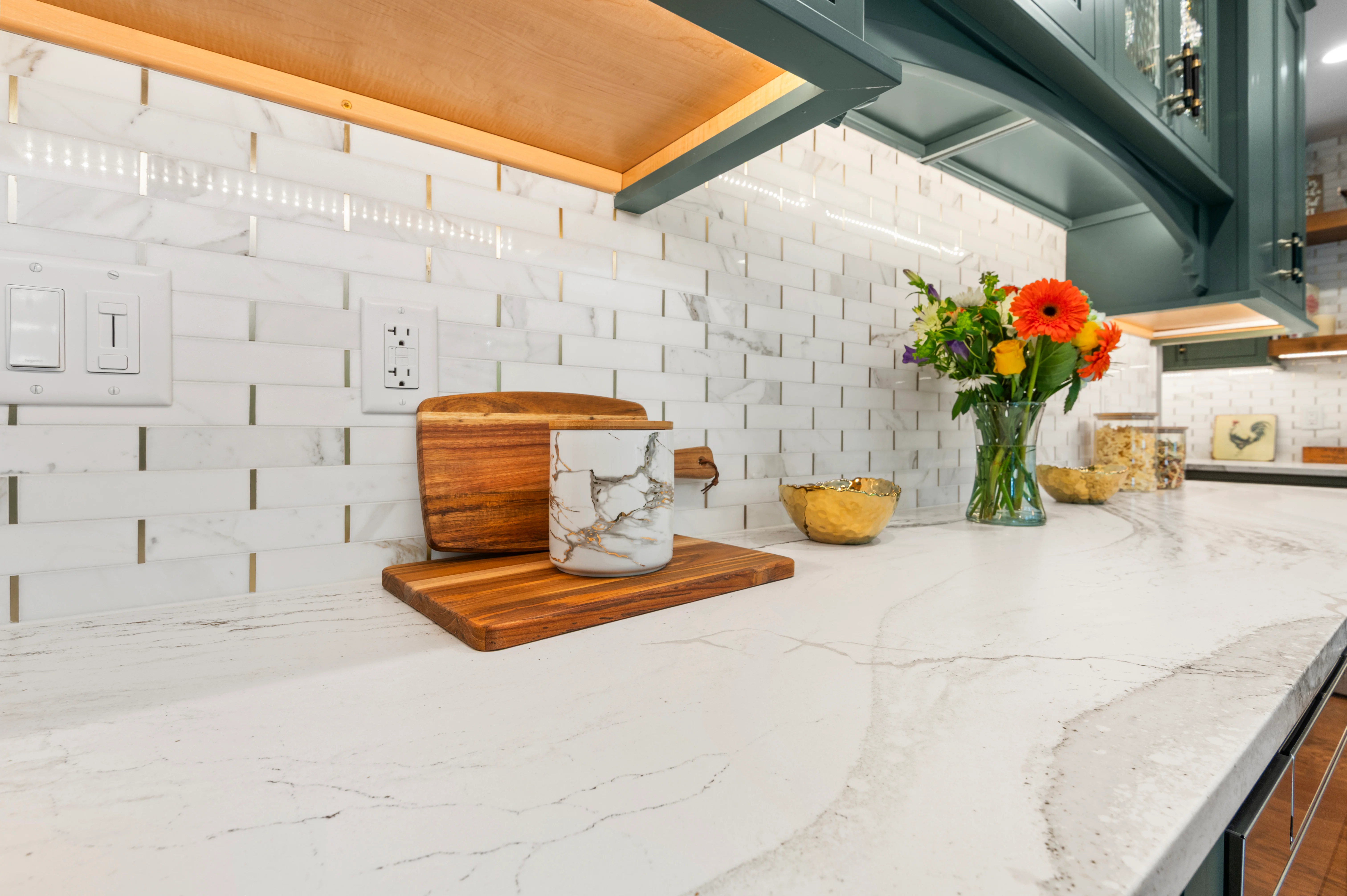 Cambria Windsor Brass quartz countertop beneath green cabinets and gold-tone lighting