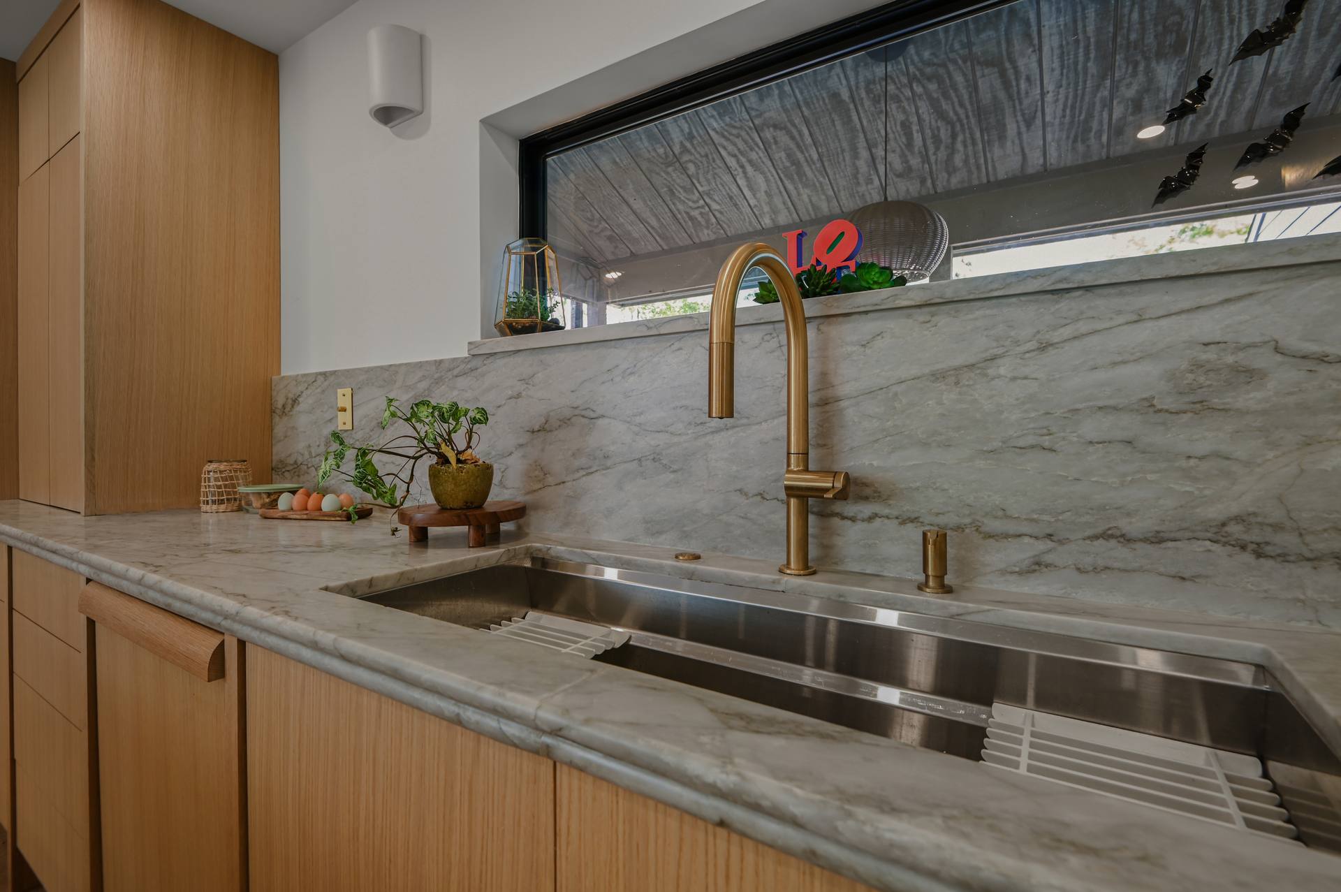 Stainless workstation sink and brass faucet in Sea Pearl quartzite with a matching backsplash