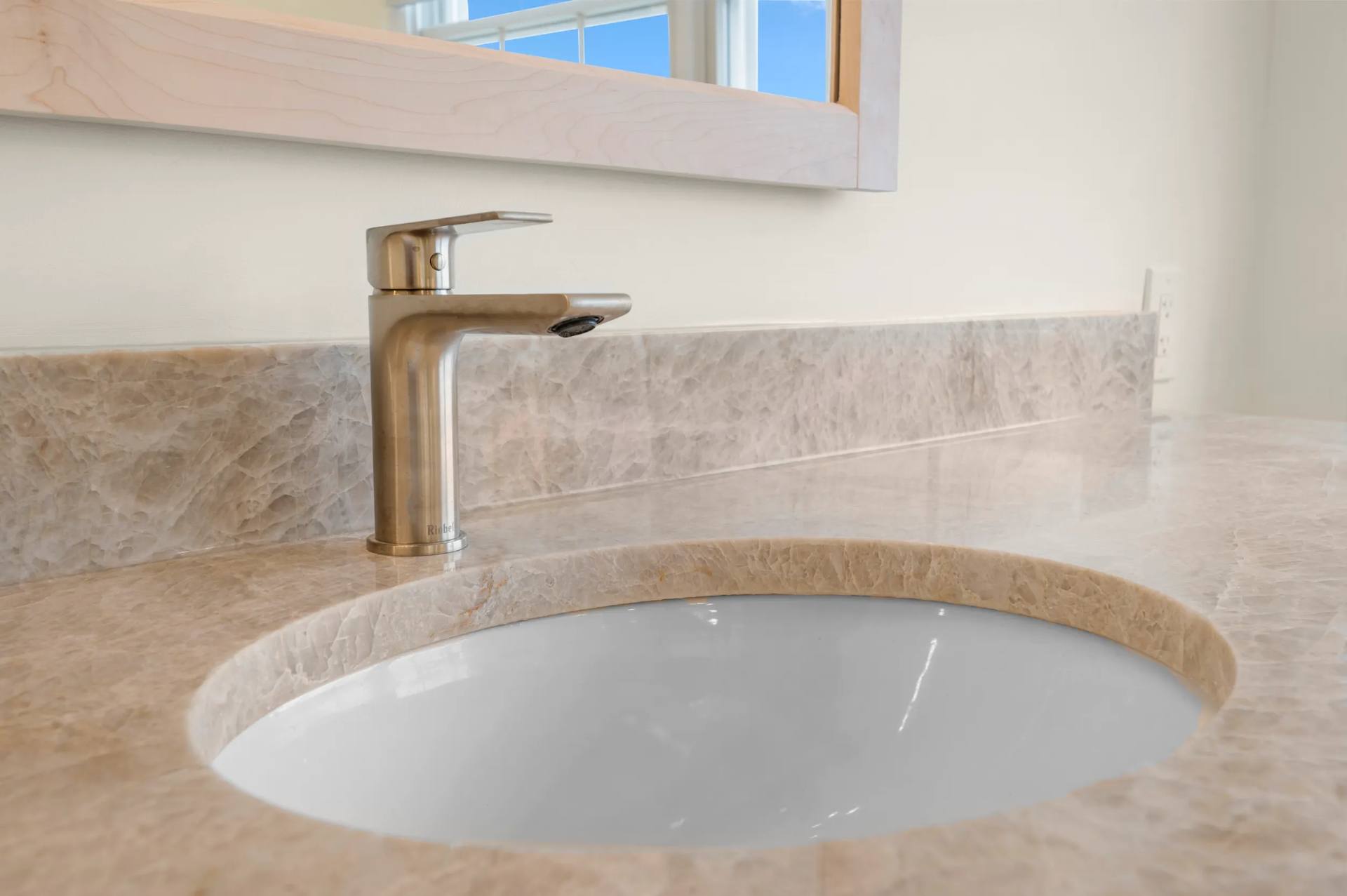 Silver-tone faucet above an undermount basin in Taj Mahal quartzite