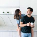 Smiling,Latin,Woman,Looking,At,Boyfriend,While,Sitting,On,Kitchen